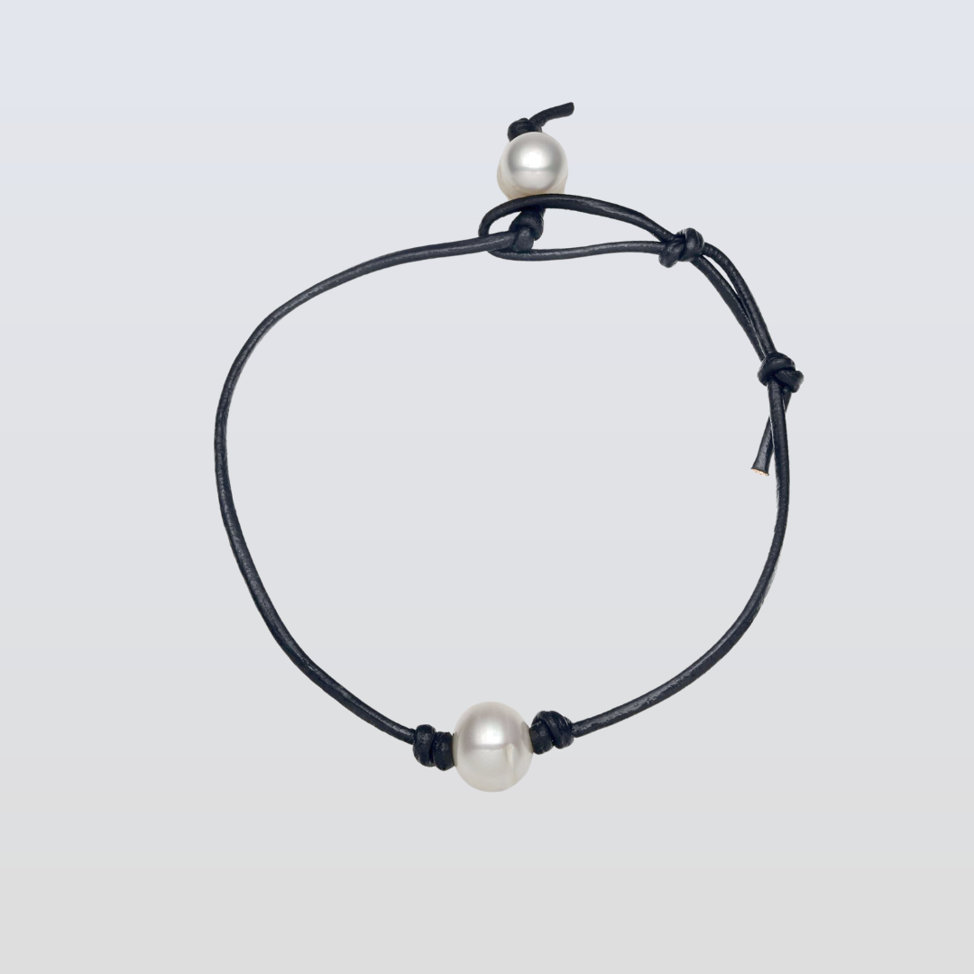 Black cord bracelet with white pearls on a light gray background