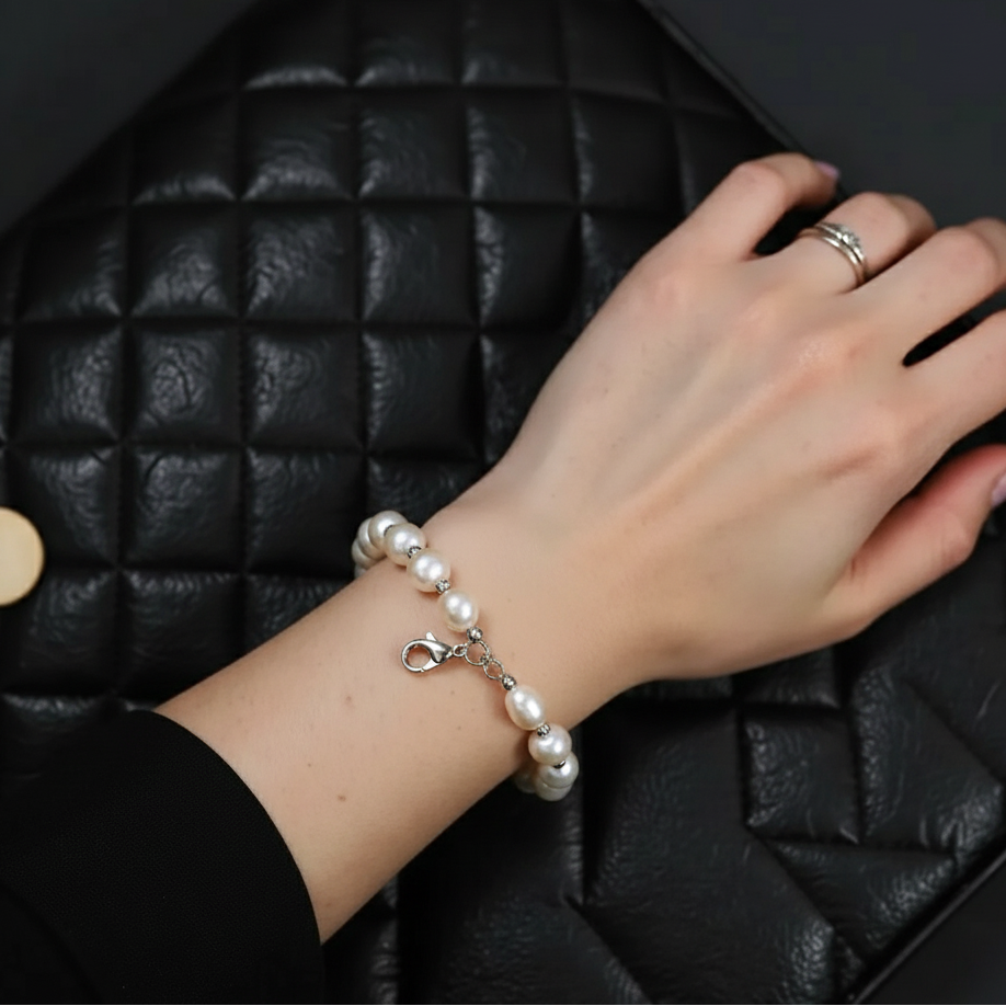 Hand wearing a pearl bracelet on a black textured surface