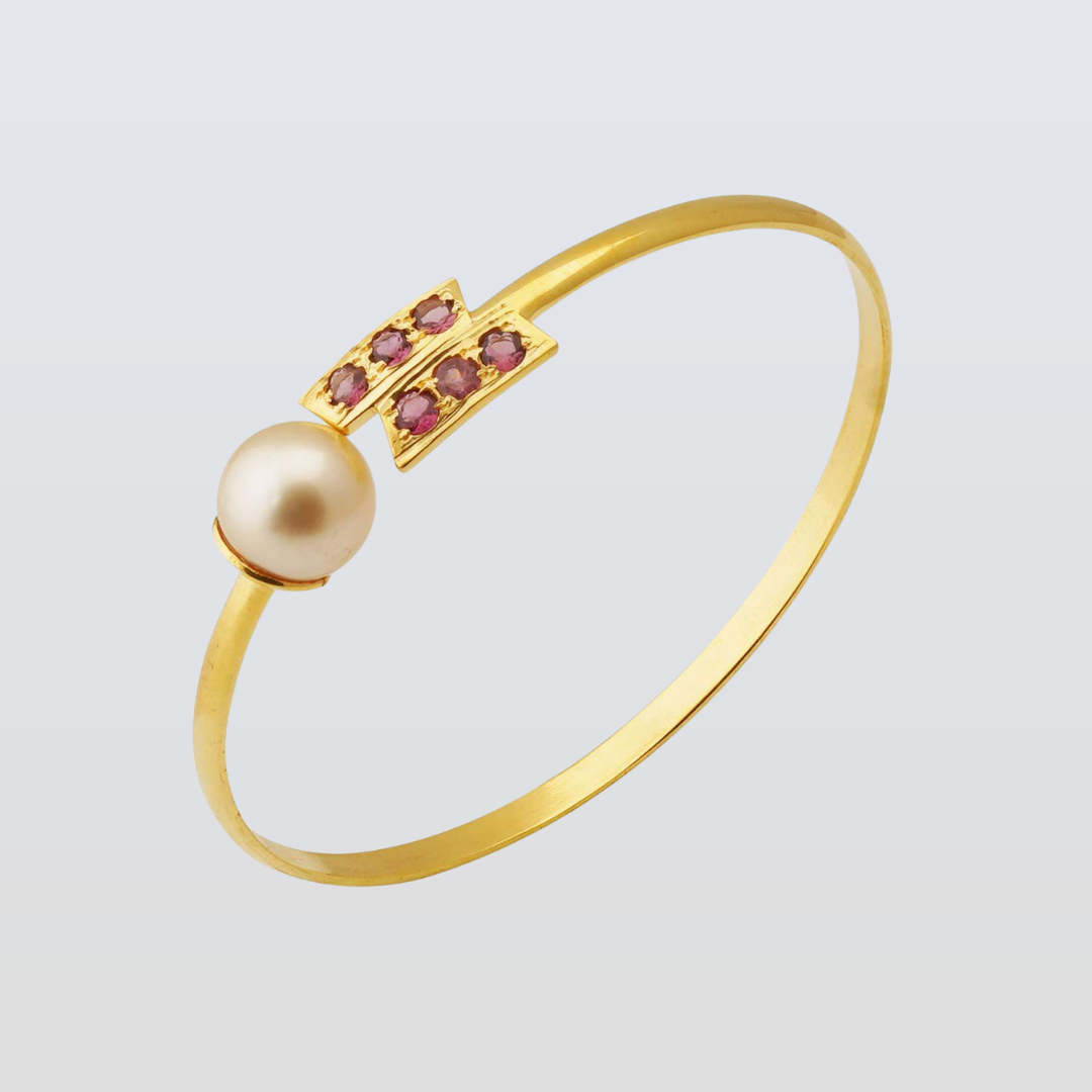 Gold bracelet with a pearl and red gemstones on a light gray background