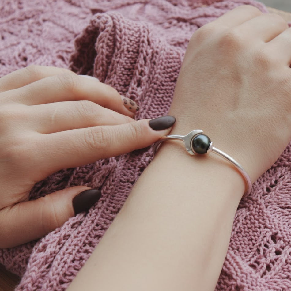 Hand wearing a silver bracelet with a black bead on a pink textured fabric background