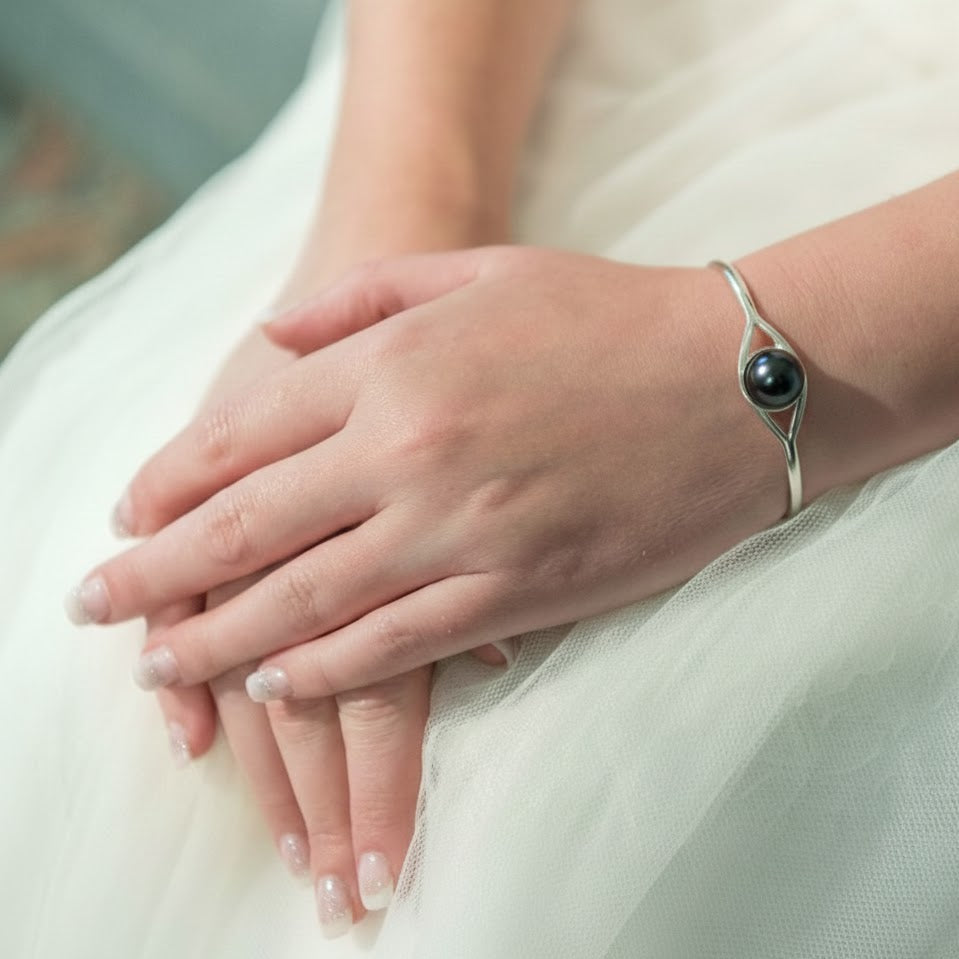 Close-up of a hand wearing a silver bracelet with a black bead on a white fabric background