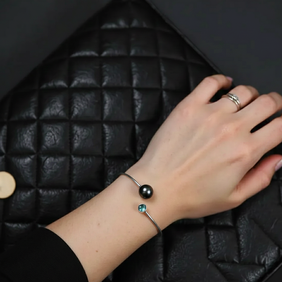 Hand wearing a bracelet with a black bead on a black textured surface