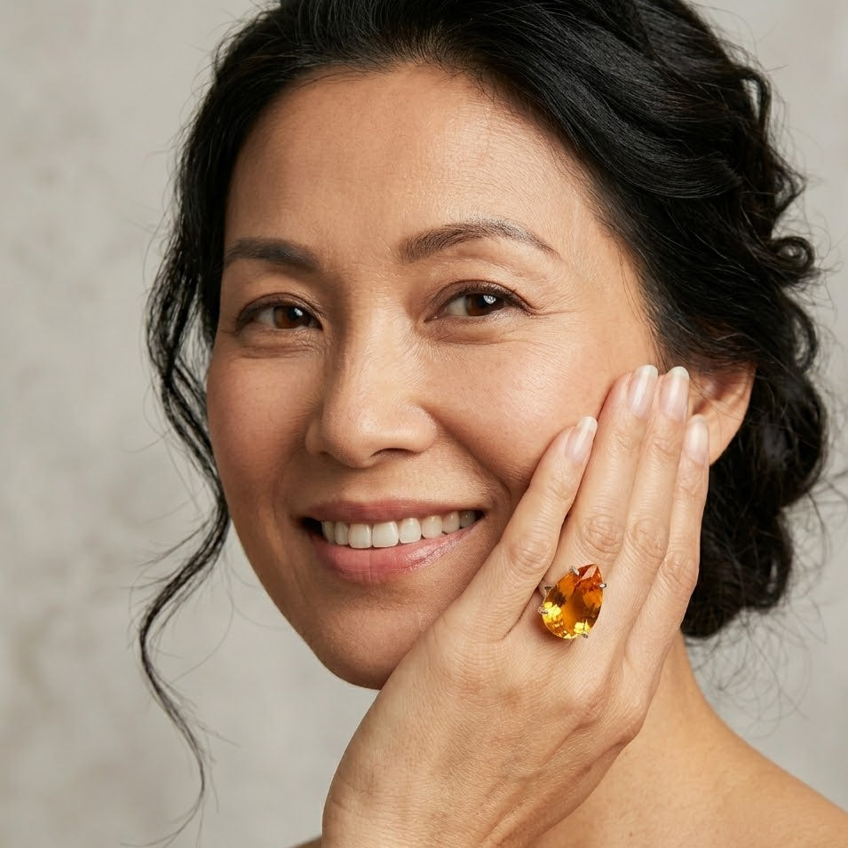 Woman wearing a large amber-colored gemstone ring on a neutral background