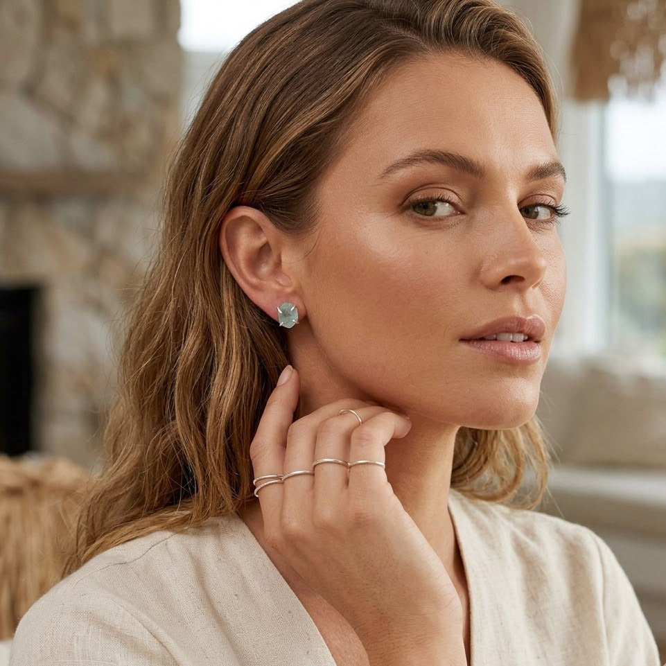 Woman wearing earrings and rings, with a blurred indoor background