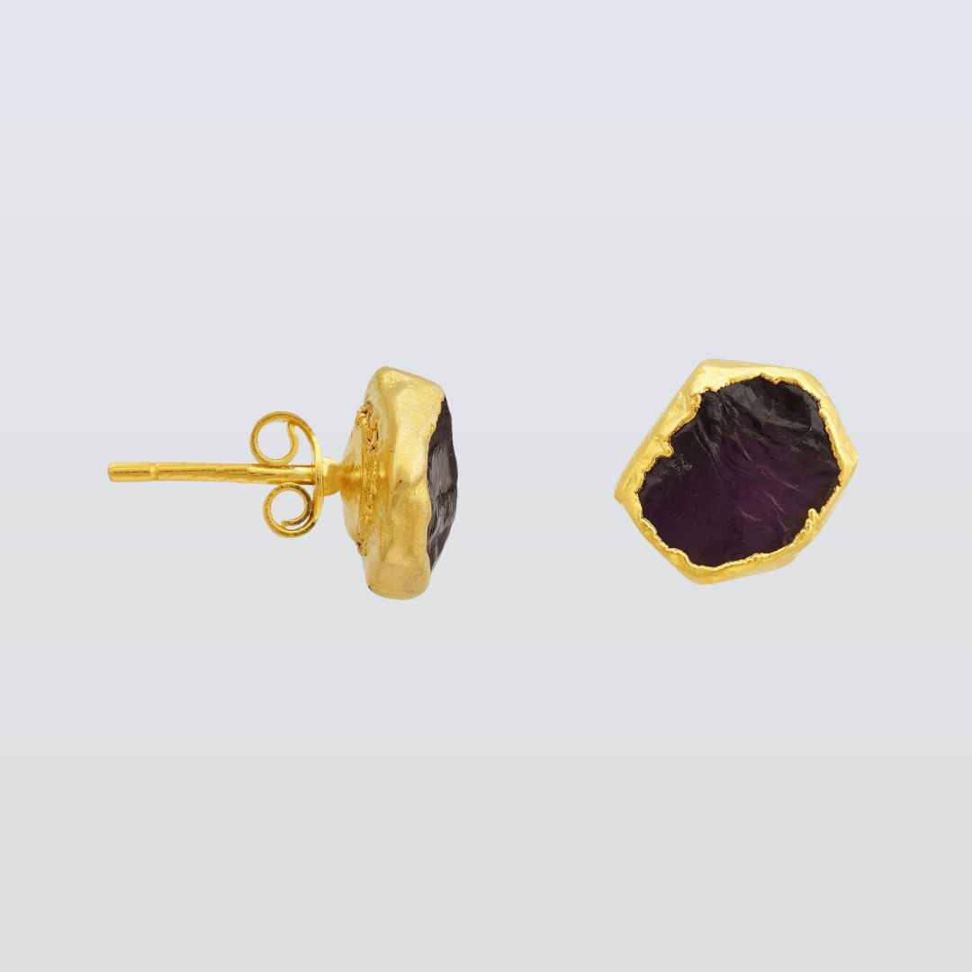 Gold earrings with purple gemstones on a light gray background