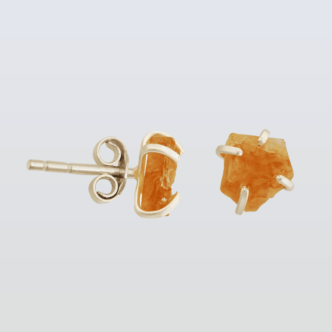 Gold stud earrings with orange gemstones on a light gray background