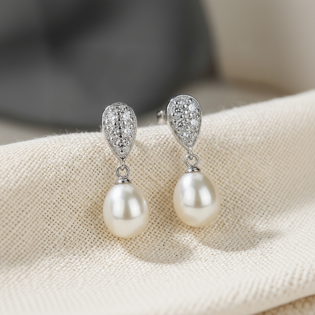 Pearl earrings with silver teardrop designs on a beige fabric background