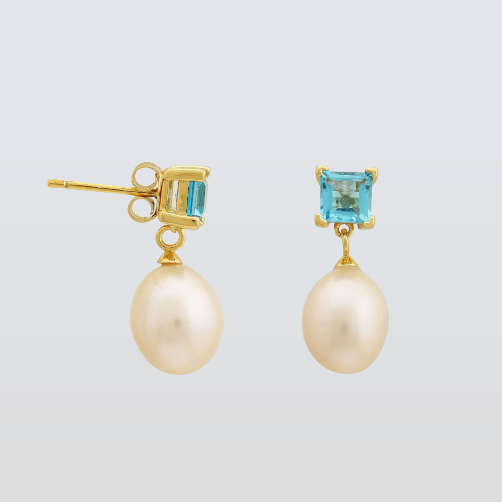 Pair of pearl earrings with gold and blue gemstone accents on a light gray background