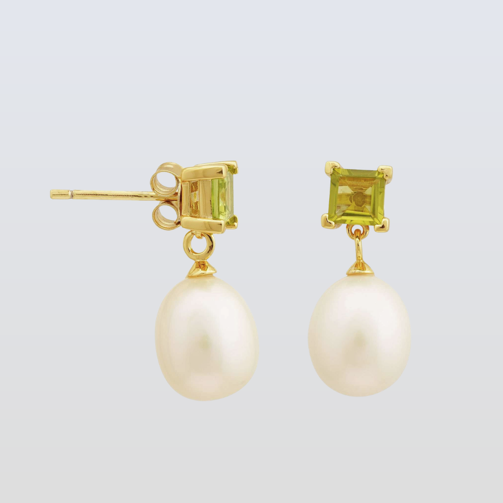 Gold earrings with pearl drops and green gemstones on a light gray background