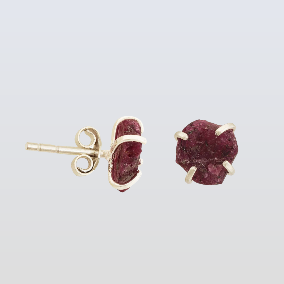 Gold earrings with red gemstones on a light gray background