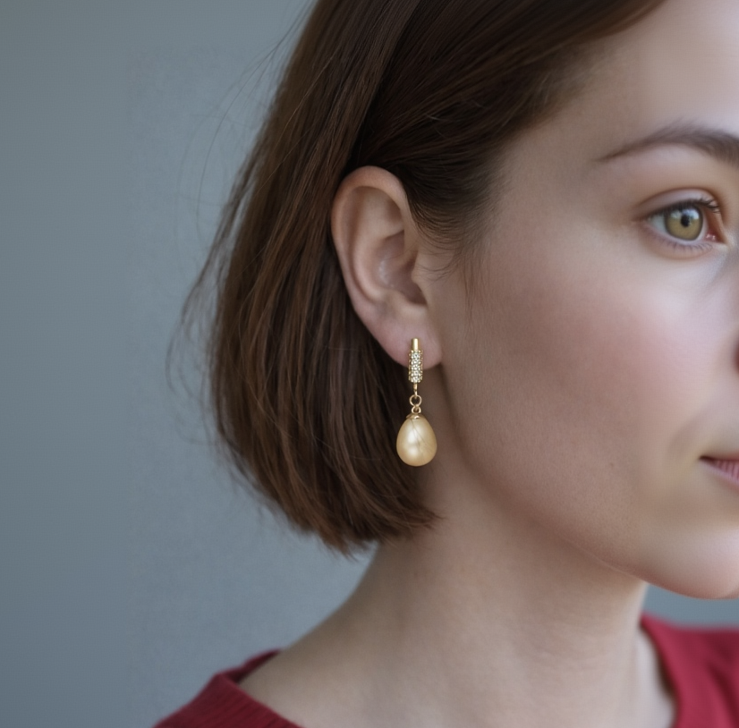 Close-up of a person wearing a gold earring with a pearl drop against a neutral background