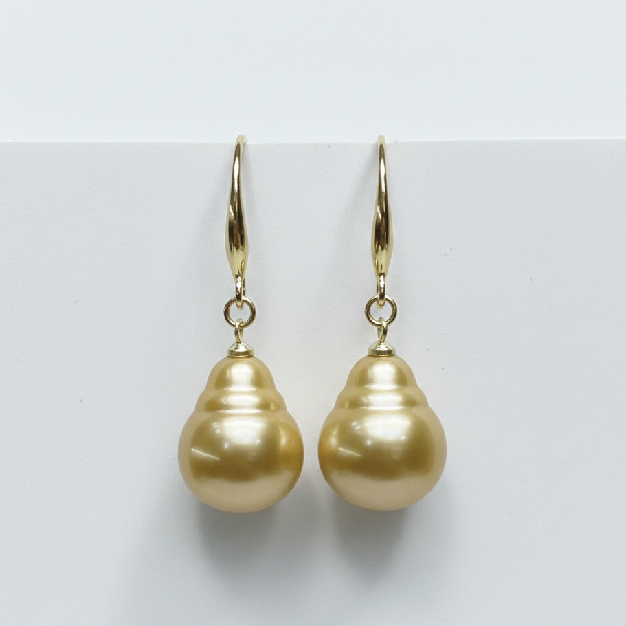 Pair of gold pearl earrings on a light gray background