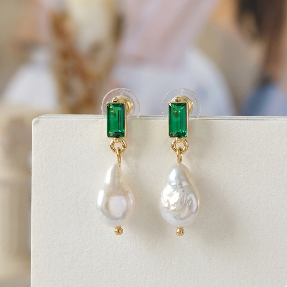Pair of earrings with emerald green gemstones and pearl drops on a white surface.