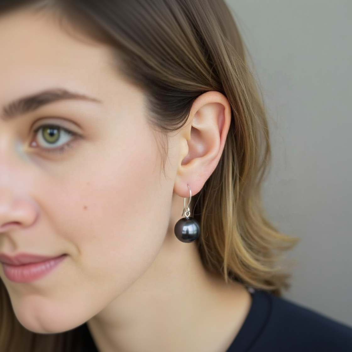 Close-up of a woman wearing a black pearl earring with a neutral background
