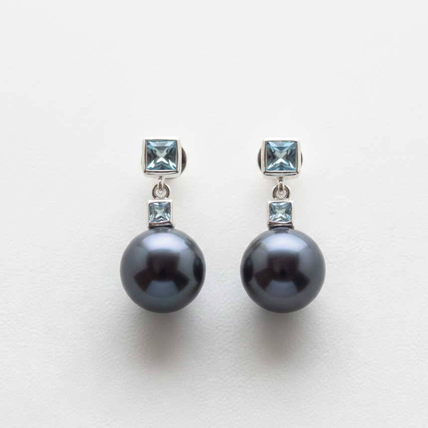 Pair of pearl earrings with gemstone accents on a light gray background
