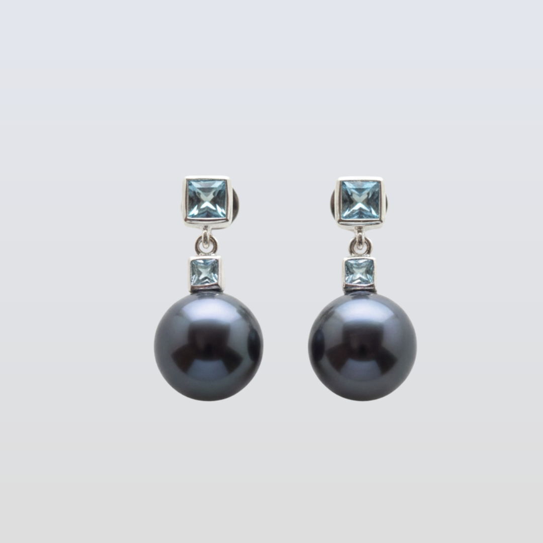 Pair of black pearl earrings with square gemstones on a light gray background