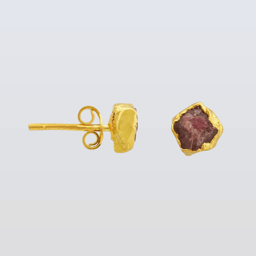 Gold earring with a red gemstone on a light gray background