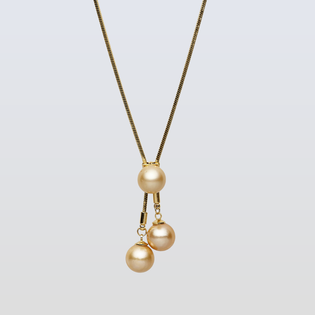 Gold necklace with three pearl pendants on a light gray background