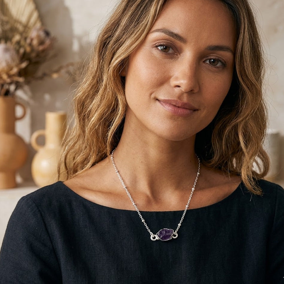 Woman wearing a necklace with a purple gemstone in a warm, indoor setting.