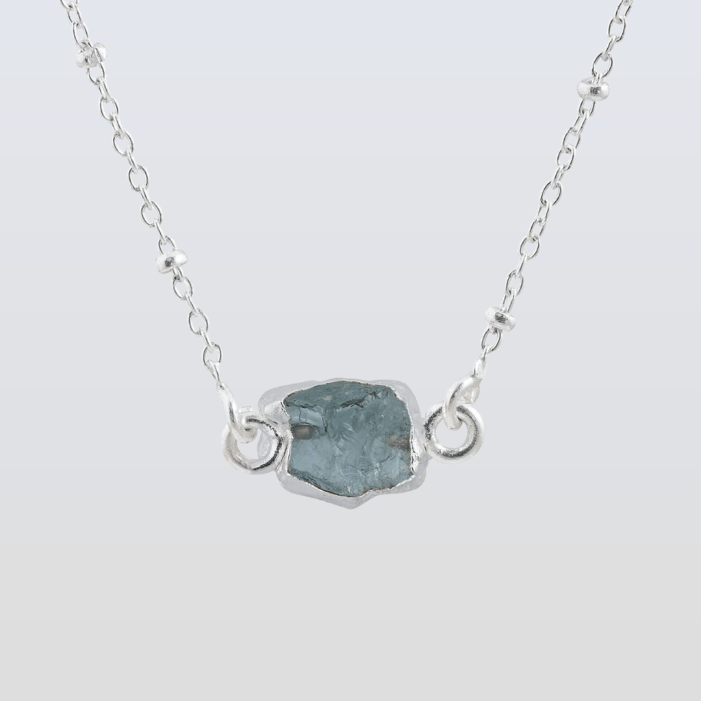 Necklace with a silver chain and a central rough-cut gemstone on a light gray background