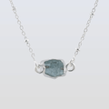 Necklace with a silver chain and a central rough-cut gemstone on a light gray background