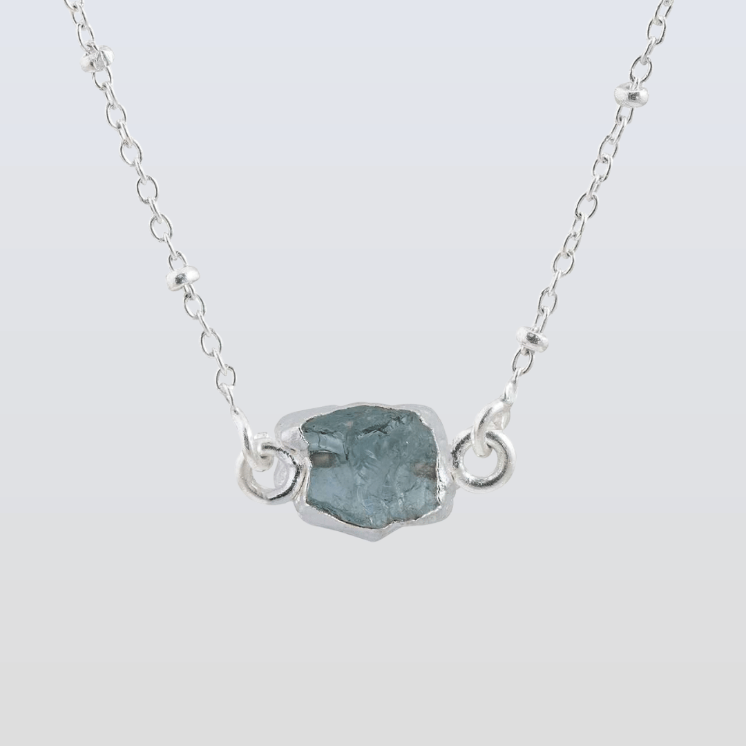 Necklace with a silver chain and a central rough-cut gemstone on a light gray background