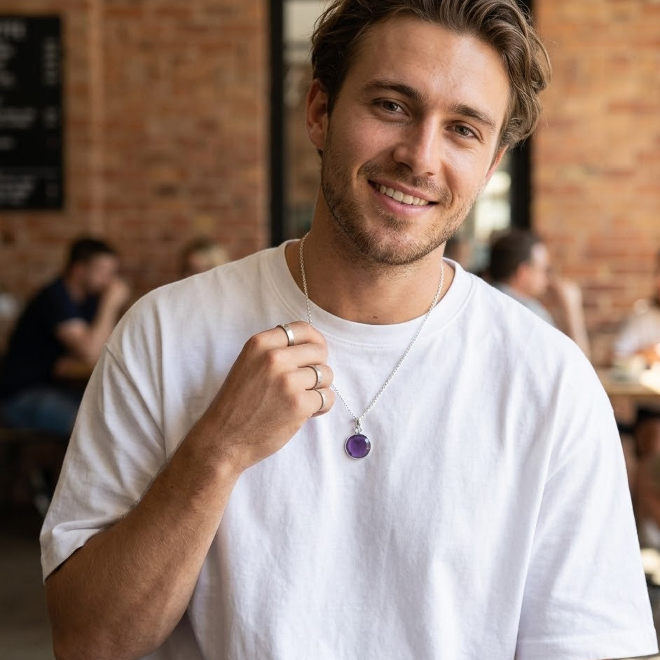 Man wearing a white t-shirt with a purple pendant in a casual setting