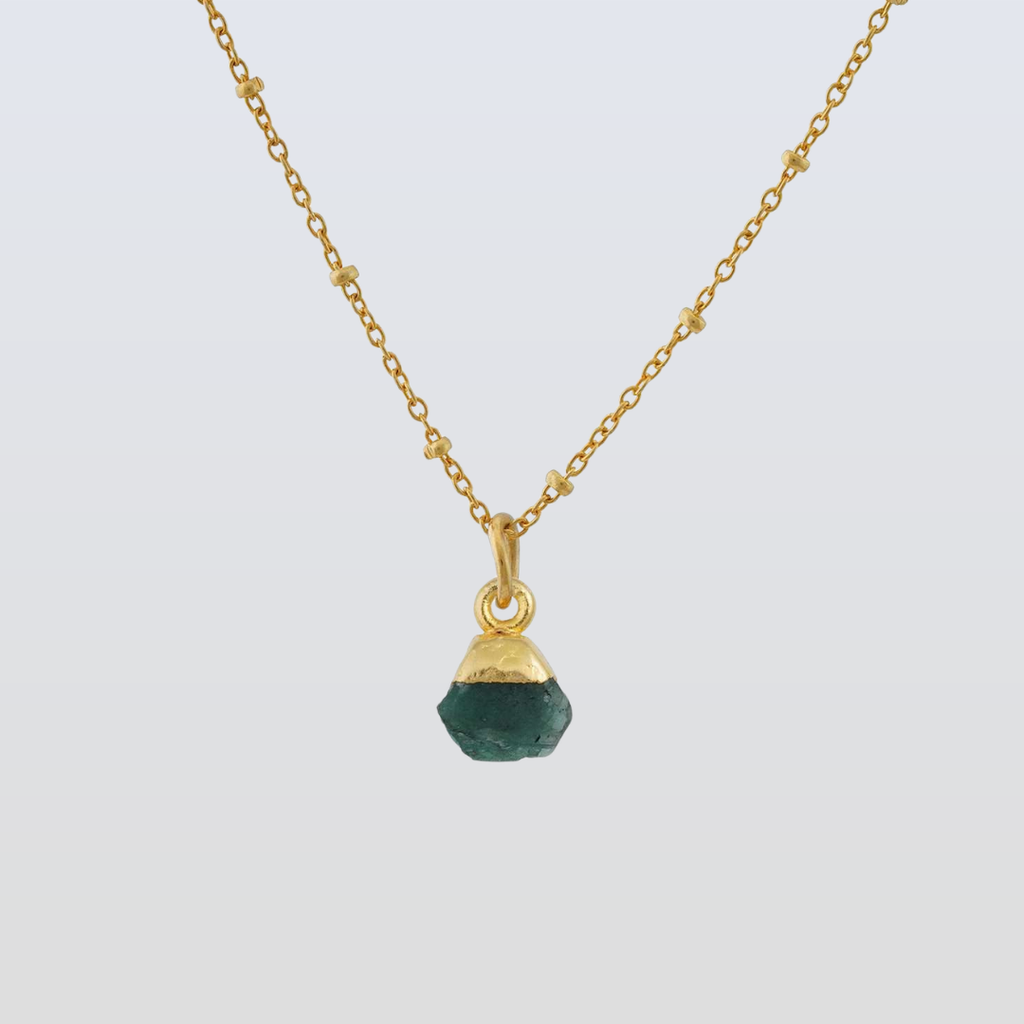 Gold necklace with a green gemstone pendant on a light gray background