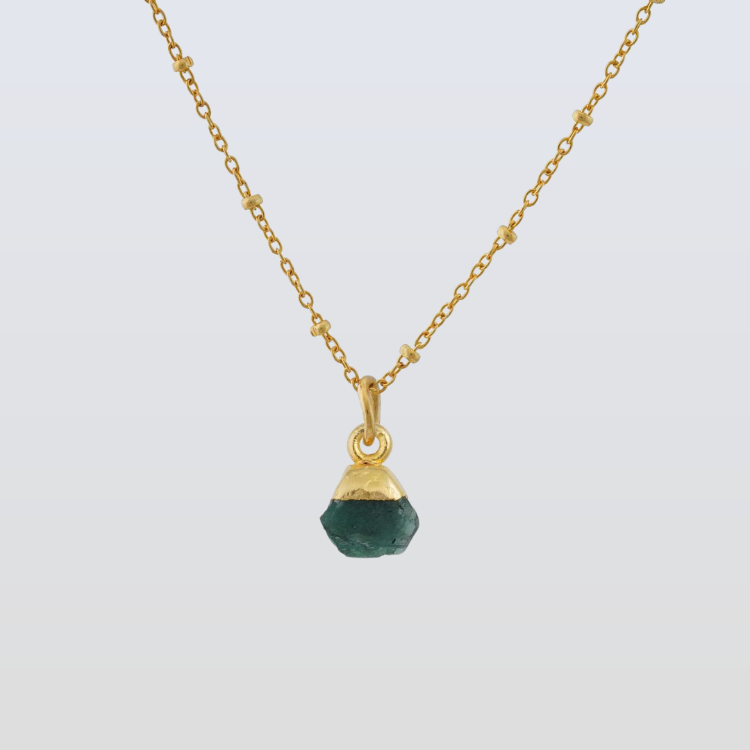 Gold necklace with a green gemstone pendant on a light gray background