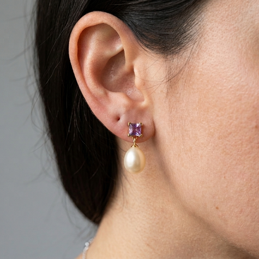 Close-up of a person wearing a gold earring with a purple gemstone and pearl drop.