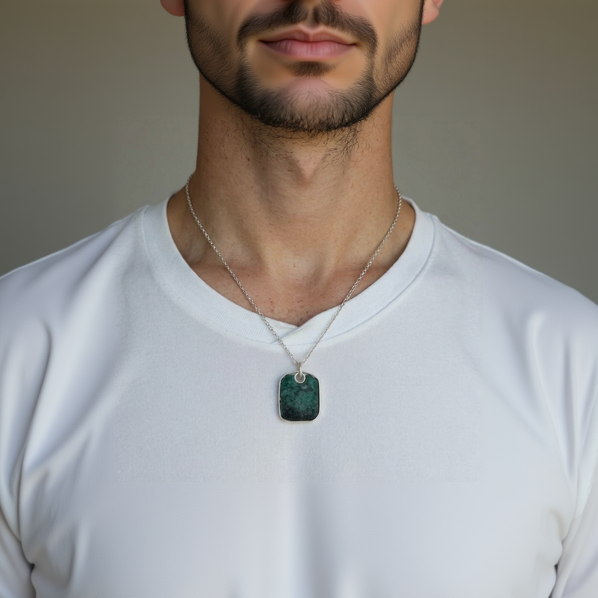 Person wearing a necklace with a green pendant on a plain background