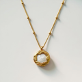 Gold necklace with a circular pendant on a light gray background
