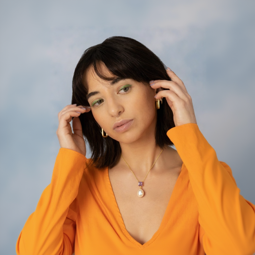 Woman wearing an orange top with a necklace against a light blue background