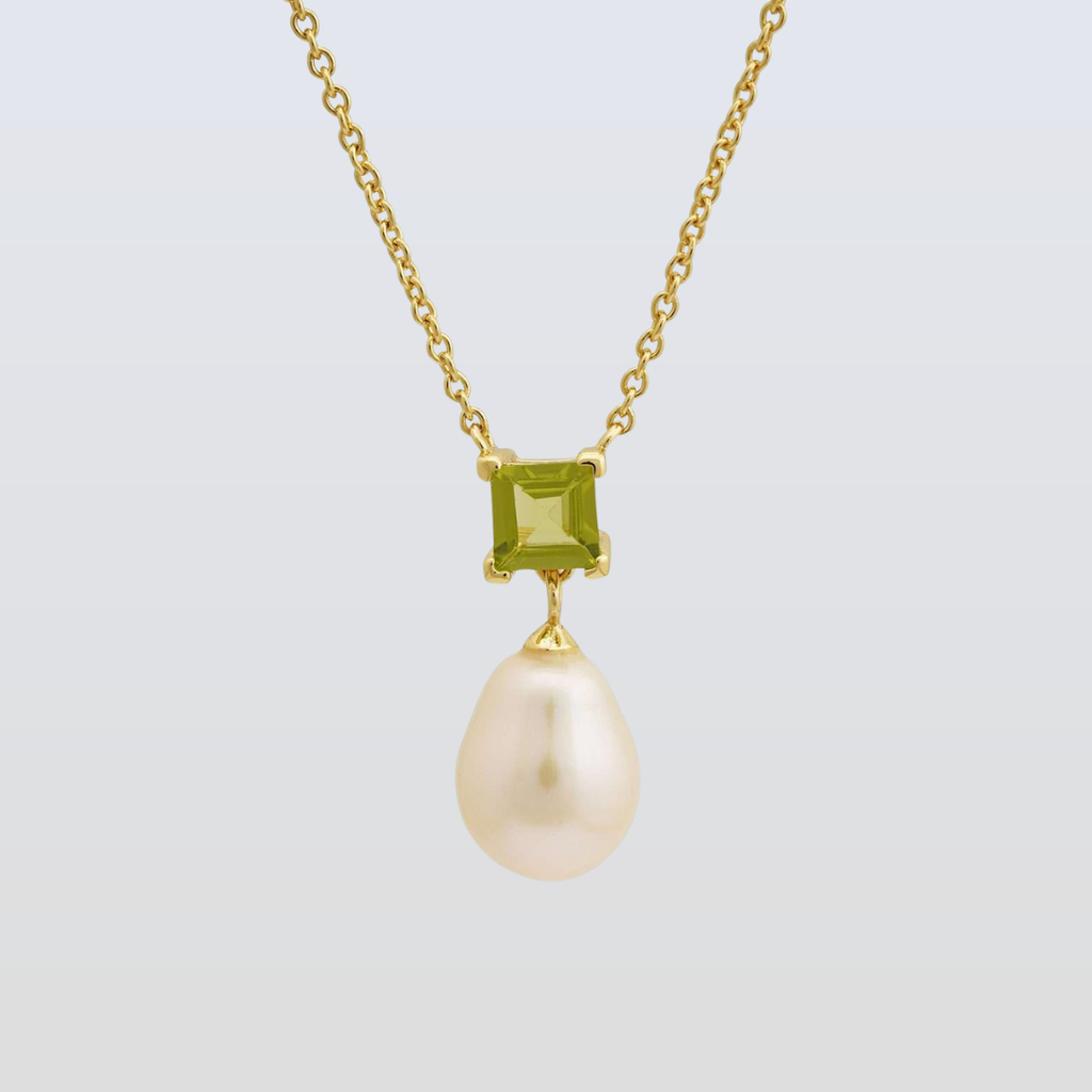Gold necklace with a green gemstone and pearl pendant on a light gray background