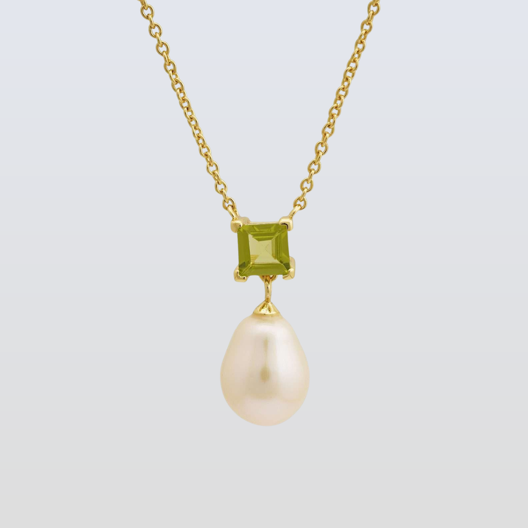 Gold necklace with a green gemstone and pearl pendant on a light gray background