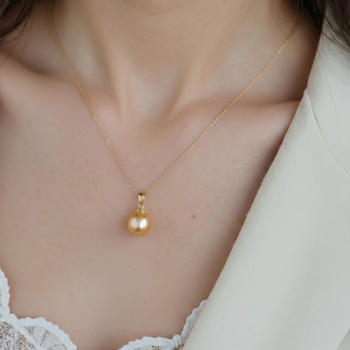 Gold necklace with a pearl pendant worn by a person in a white outfit.