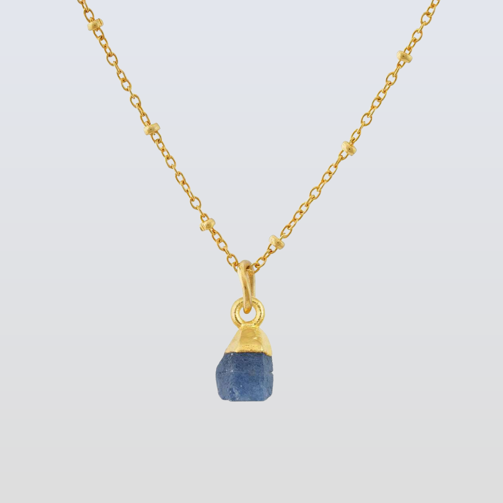 Gold necklace with a blue pendant on a light gray background
