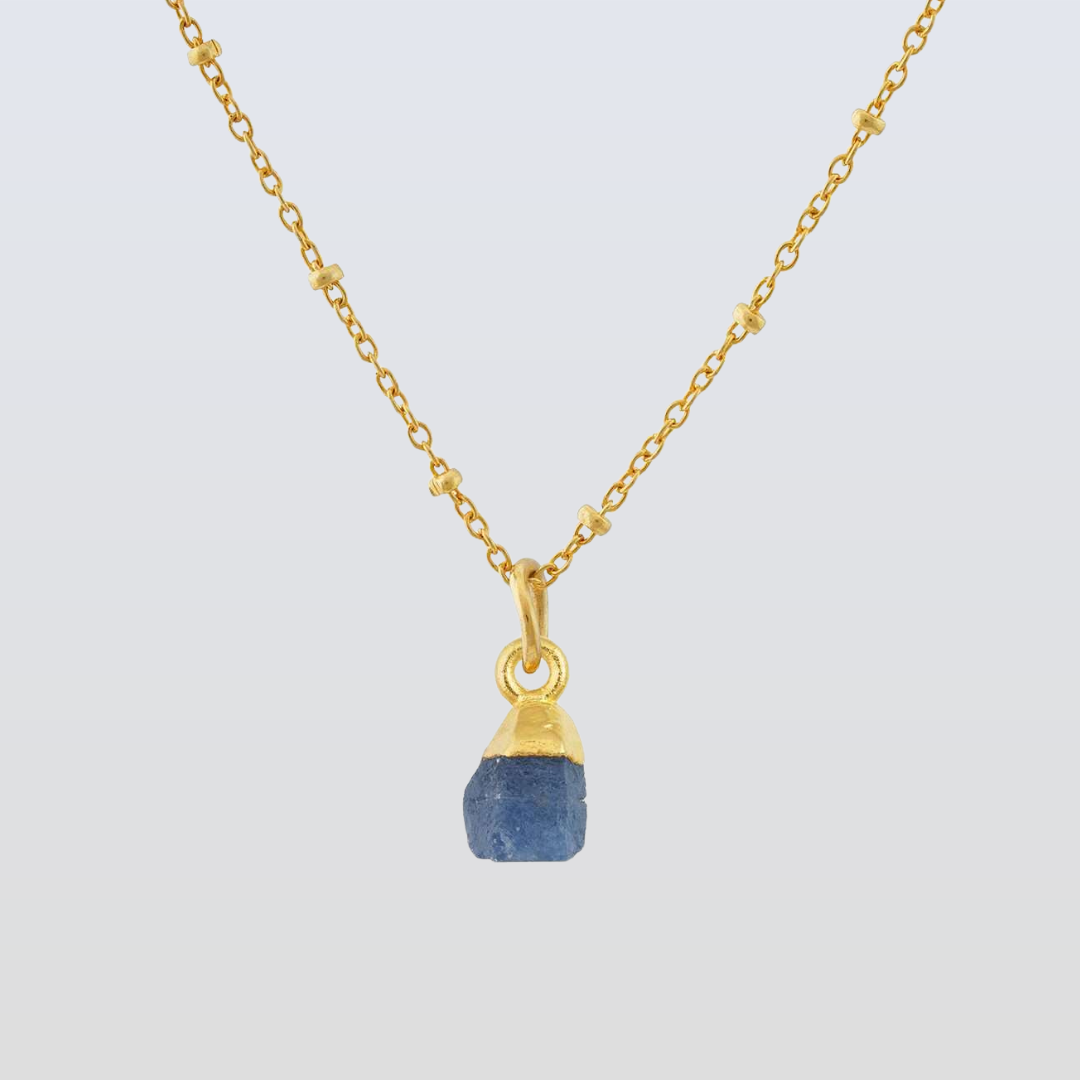 Gold necklace with a blue pendant on a light gray background