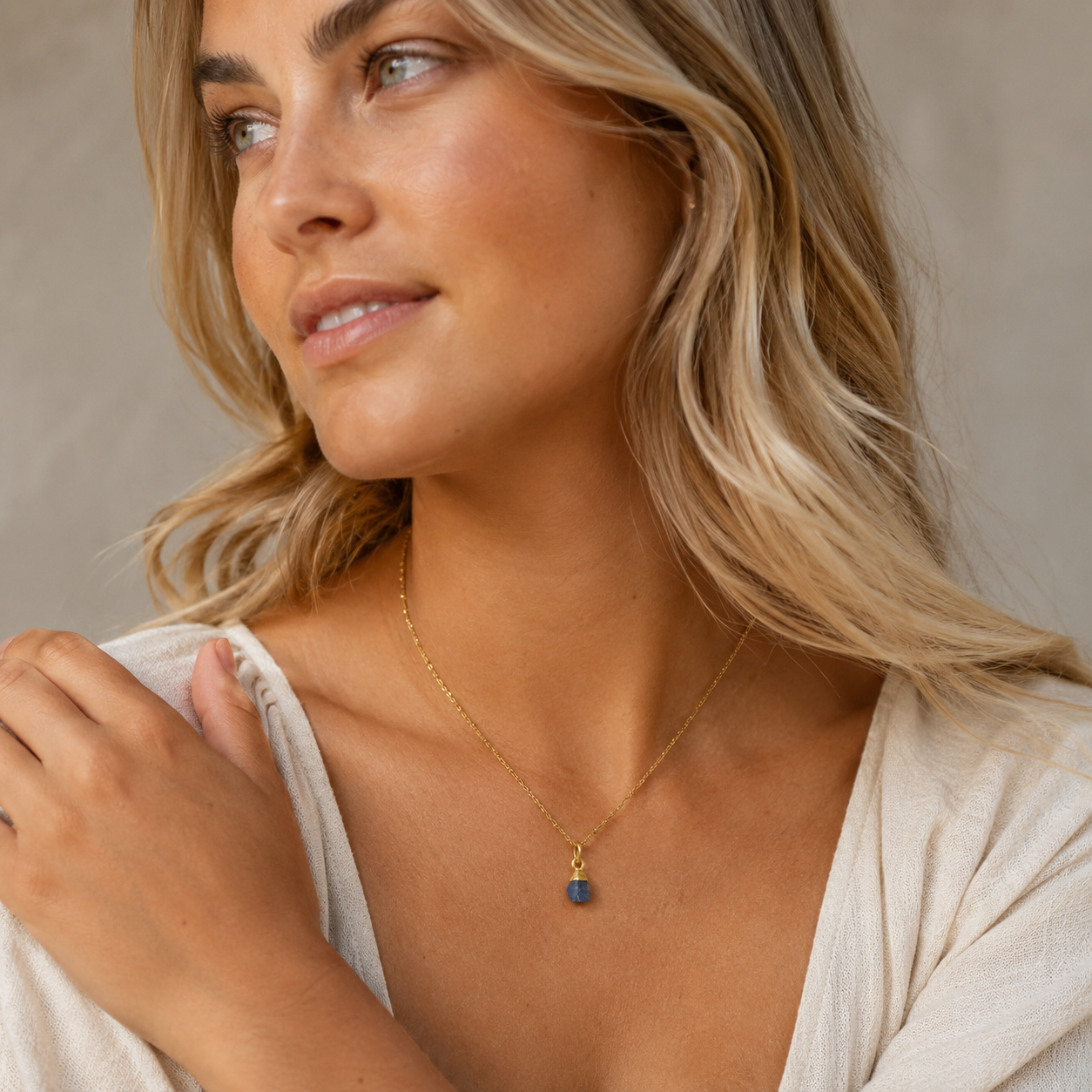Woman wearing a gold necklace with a small pendant against a neutral background