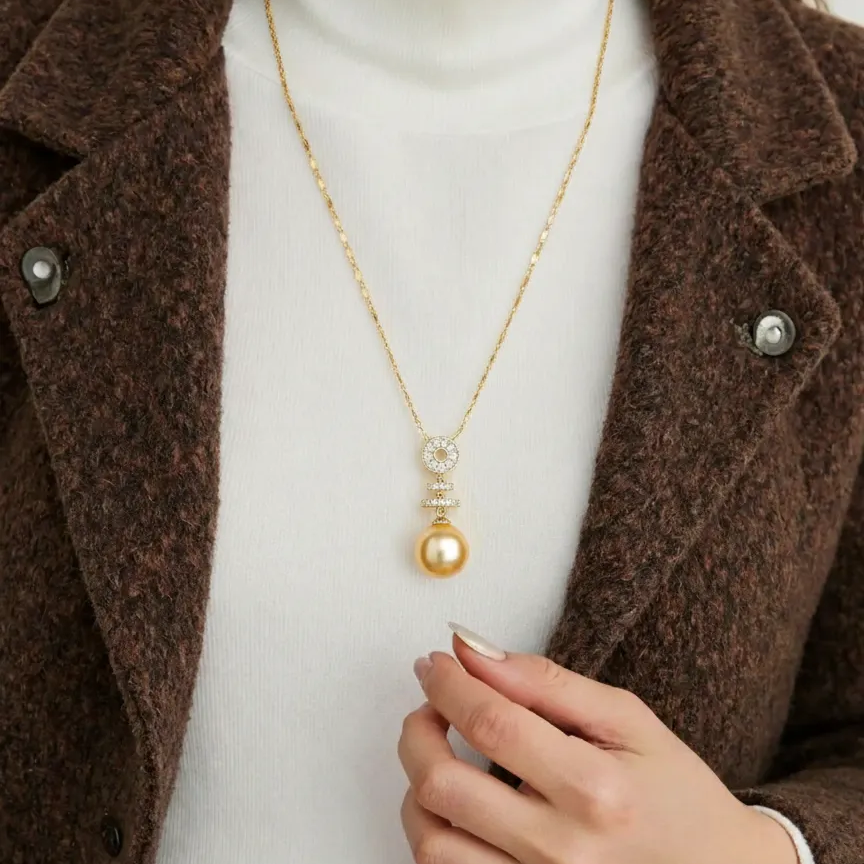 Person wearing a gold necklace with a pendant, dressed in a brown coat and white turtleneck.