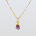Gold necklace with a purple pendant on a light gray background