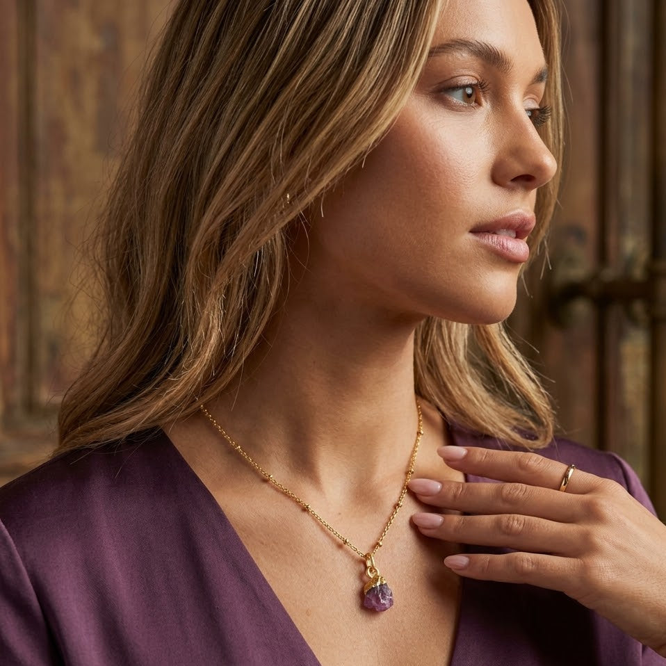Woman wearing a gold necklace with a purple pendant in an elegant setting.