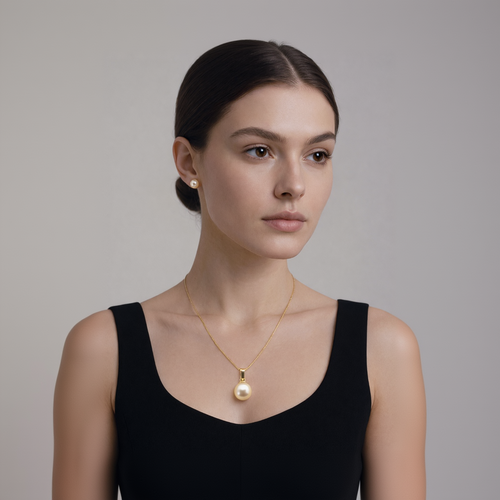 Woman wearing a gold necklace with a pearl pendant against a neutral background