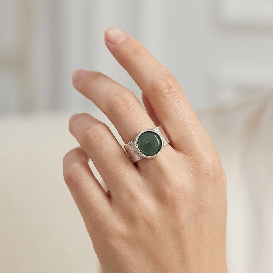 Hand wearing a silver ring with a green stone on a neutral background