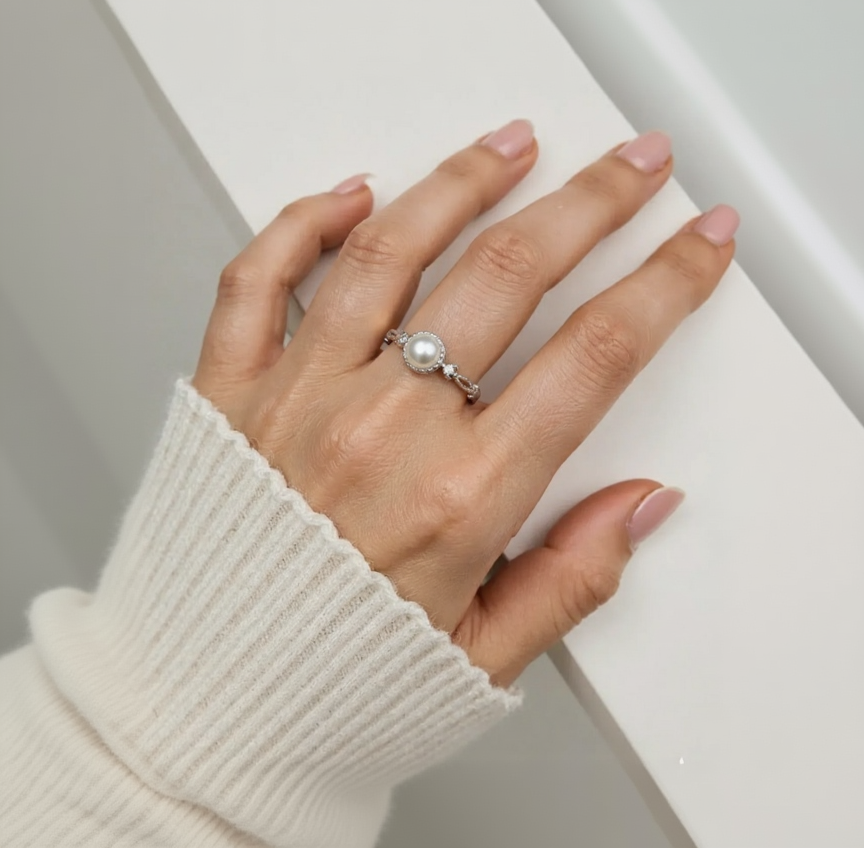 Hand wearing a silver ring with a pearl on a neutral background