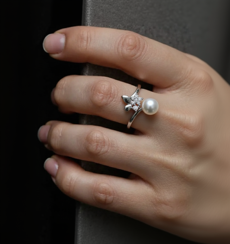 Hand wearing a silver ring with a star design and a pearl on a dark background