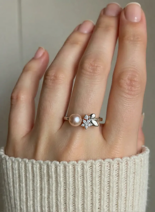 Hand wearing a ring with a pearl and floral design on a neutral background