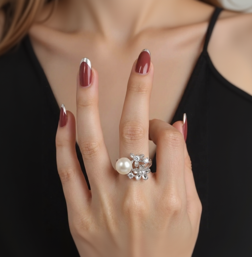 Hand wearing a silver ring with a pearl and gemstones against a neutral background