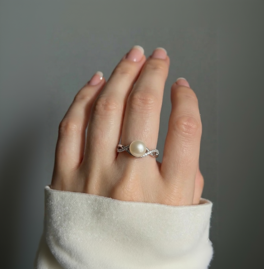 Hand wearing a pearl ring against a gray background