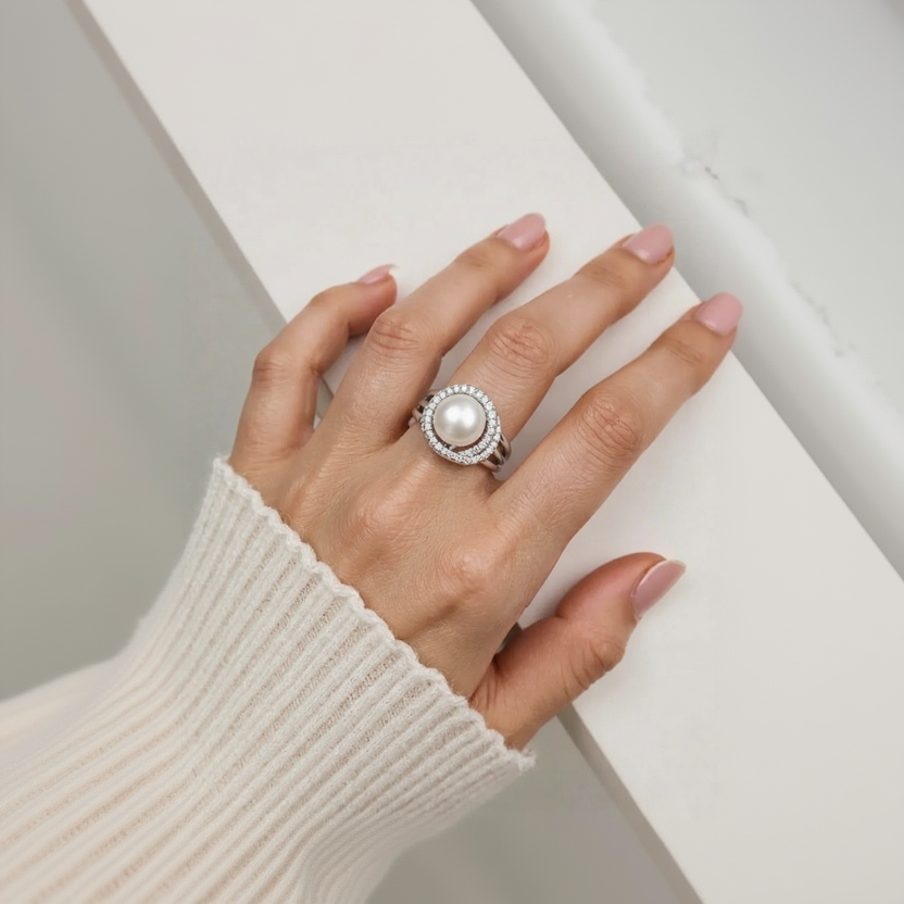 Hand wearing a pearl ring on a neutral background